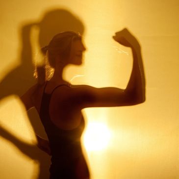 Silhouette of a woman flexing her arm against a warm backlight.