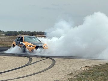 Orange car drifting, creating thick white smoke on a race track.