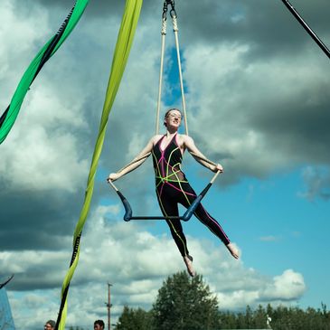Aerial performer on trapeze under cloudy sky.