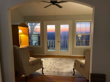 Cozy living room with patterned chairs, warm lighting, and sunset view through glass doors.