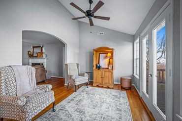 Cozy sitting area with patterned armchairs, wooden floor, and natural light from large windows.