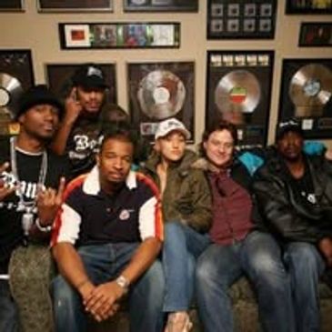 Group of five people sitting on a couch with music awards on the wall.