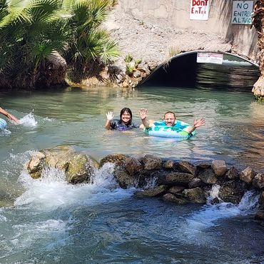 People enjoying swimming and floating in a natural water stream with greenery and signs.