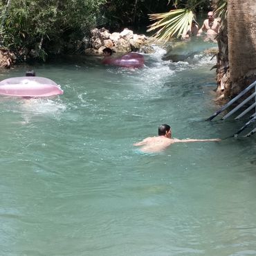 People swimming and floating in a natural water stream surrounded by trees.