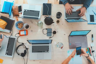 Top view of a shared workspace with laptops, gadgets, and people working.