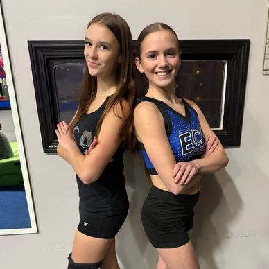 Two teenage girls in cheerleading outfits standing back-to-back with arms crossed.