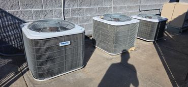 Three outdoor air conditioning units lined up against a wall on a sunny day.