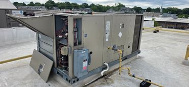 Open rooftop HVAC unit with tools on top and exposed wiring.