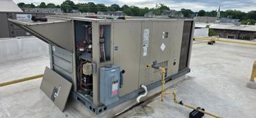 Open rooftop HVAC unit with tools on top and exposed wiring.