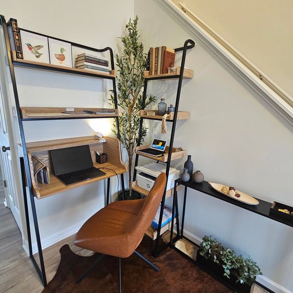 Modern workspace with wooden shelves, a brown chair, and decorative plants under a staircase.