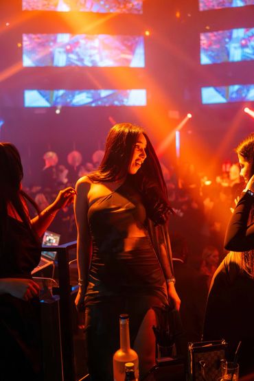 Woman in a sleek dress enjoying a vibrant nightclub scene with colorful lights.
