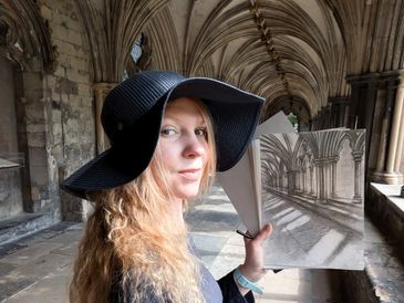 Woman in a black hat holding a drawing of an arched corridor inside the same corridor.