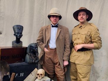 Two men in vintage explorer outfits surrounded by Egyptian artifacts and a skull.