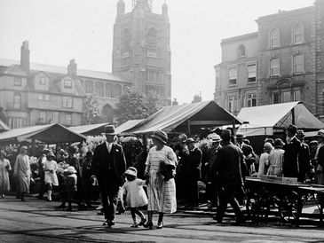 Crowd at an outdoor market in early 20th century with people in period attire.