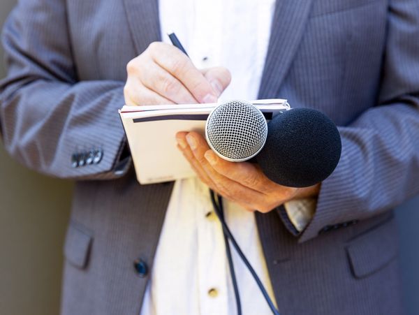 A journalist holding a microphone and taking notes