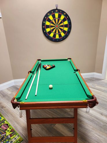 A billiard table with balls and cues, and a dartboard hanging on the wall.