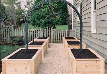 Wooden raised garden beds with soil and metal arch trellises in a backyard.