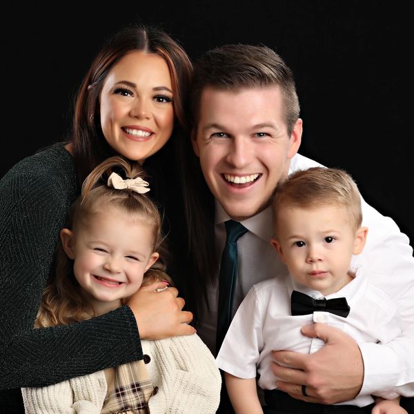 Young man in a tie hugging a woman in a black dress and two children, one girl and one boy
