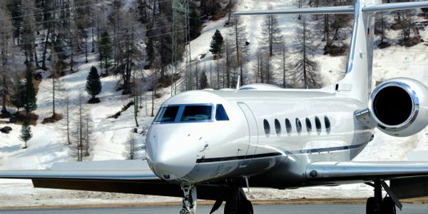 Private jet parked on a snowy runway with forested hills in the background.