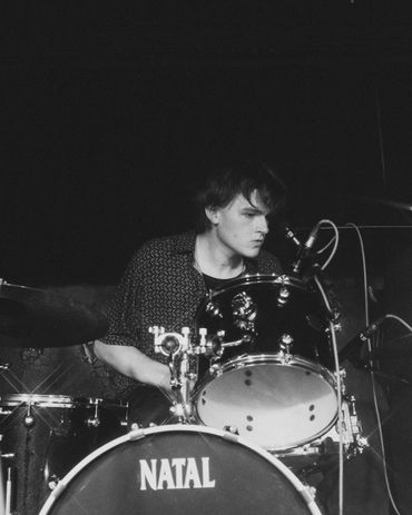 A focused drummer playing a Natal drum set in a dark setting.