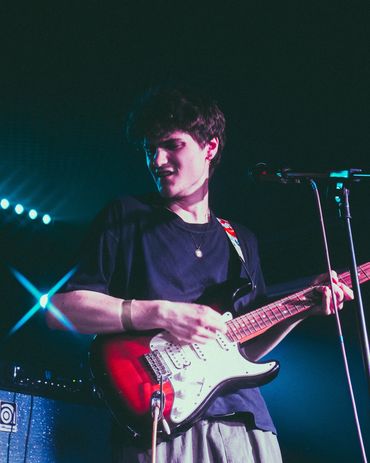 Young man passionately playing electric guitar on stage with colorful lights.