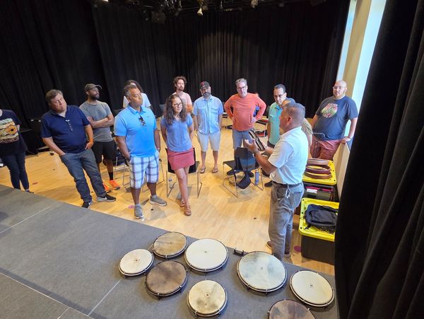 Grupo escuchando charla en aula con tambores en primer plano.