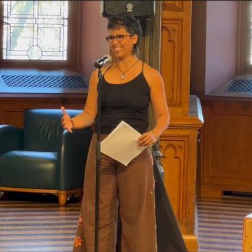 Person speaking into a microphone, holding a paper.