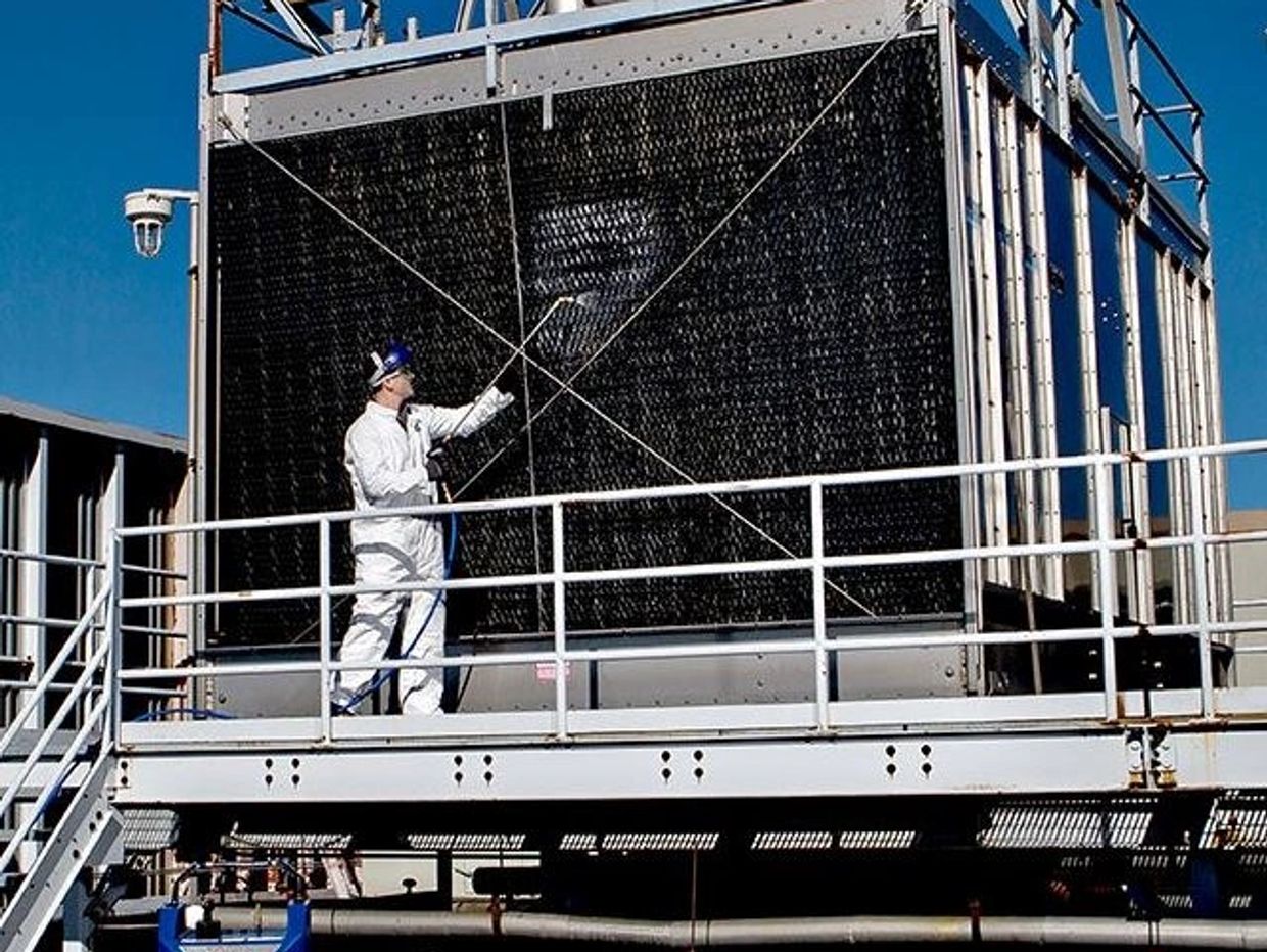 Worker in protective gear inspecting industrial cooling equipment outdoors.