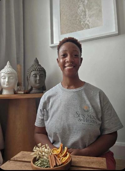 Smiling woman with herbal ingredients and Buddha statues.