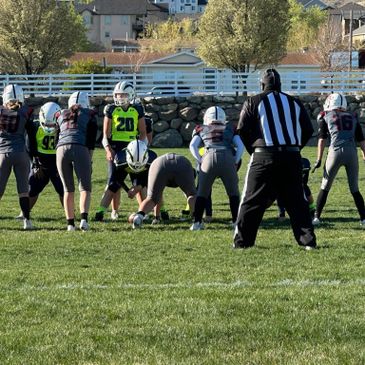 Youth football teams line up for a play under referee supervision on a sunny day.