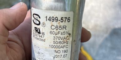 Hand holding a metal capacitor with specifications and label.