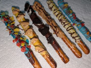 Six decorated pretzel rods with colorful toppings on a white paper towel.