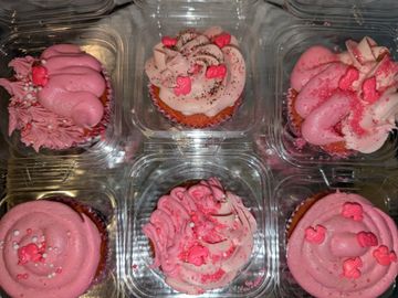 A box of six pink-frosted cupcakes with decorative sprinkles and candies.