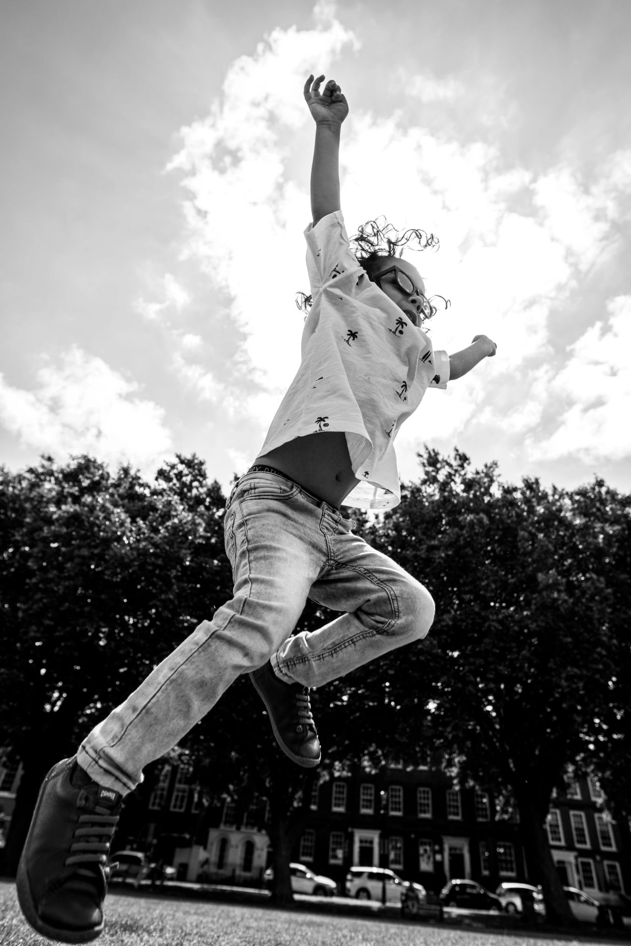 Child joyfully jumps outdoors with arms raised.