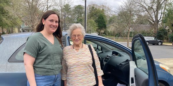 A member and volunteer standing outside a car