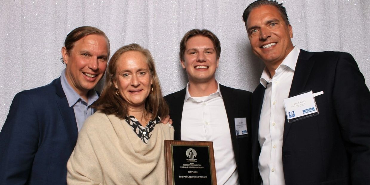 Four smiling people holding an award plaque at a formal event.