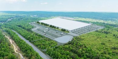 A large warehouse surrounded by forest and roads under a bright sky.