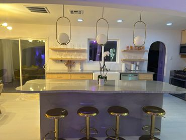 Modern kitchen with marble island, gold stools, and elegant lighting.