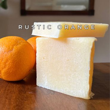 Rustic orange soap bar with fresh oranges on wooden surface.