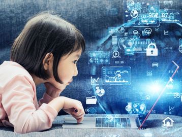 Young child looks at a laptop as digital icons and data graphics appear around the screen.