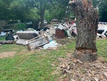 Outdoor pile of discarded furniture and debris under trees.