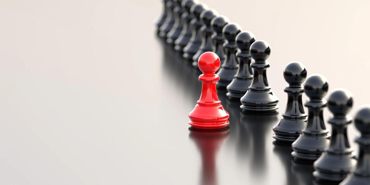 A red chess pawn stands out in front of black pawns in a row.