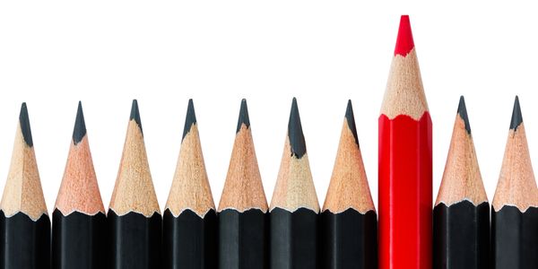 A red pencil stands out among black pencils in a row.
