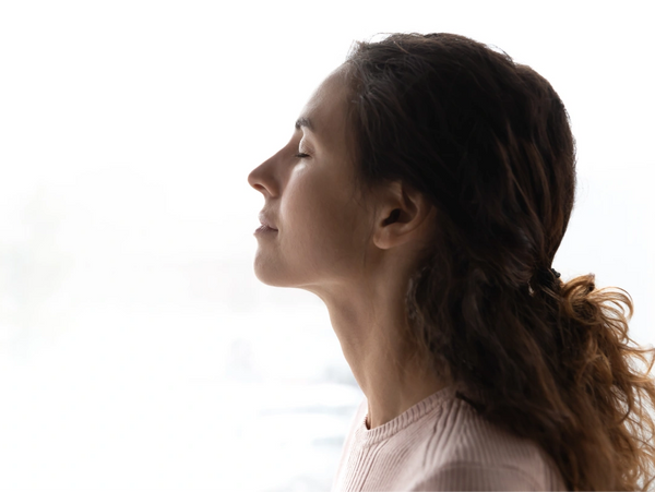 A serene woman in profile, eyes closed, head slightly tilted up, with dark wavy hair tied back.