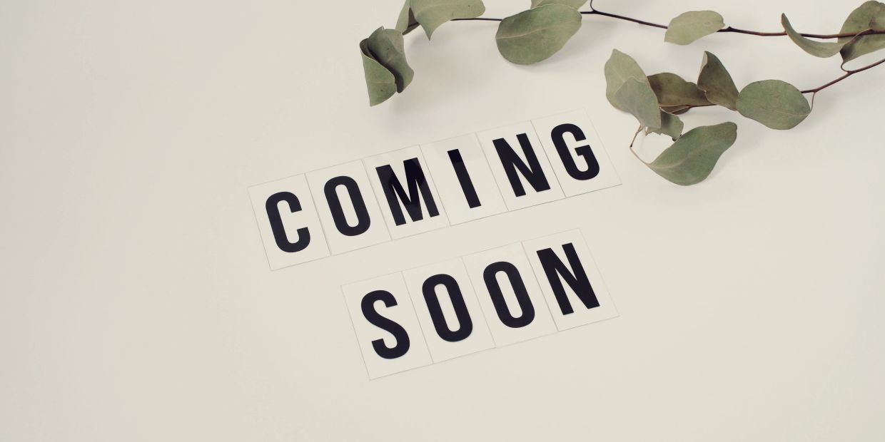 Schilder mit Text 'Coming Soon' und grünem Blattzweig.
