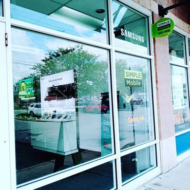 Storefront window displaying Samsung and Simple Mobile advertisements with reflections of cars and trees.