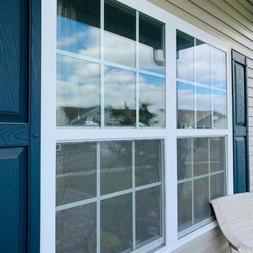 White-framed window with blue shutters reflecting a cloudy sky and nearby houses.
