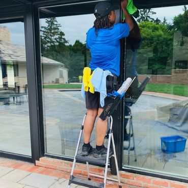 Person cleaning a large glass window outdoors using a green cloth.