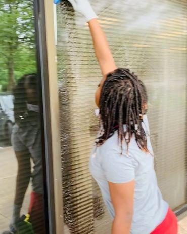 Child with braided hair cleaning a glass window outdoors.