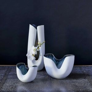 Three modern white ceramic vases with a dark interior, one holding white orchids.